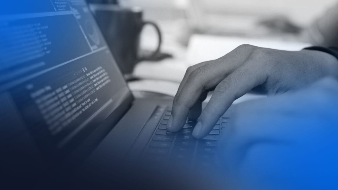 Pessoa digitando código em notebook com tela de programação, representando atualização de sistemas para adequação ao cnpj alfanumérico.