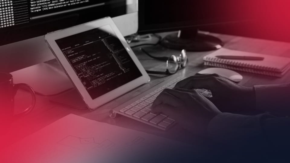 Profissional digitando código em computador e tablet, simbolizando análise e atualização de códigos legados.