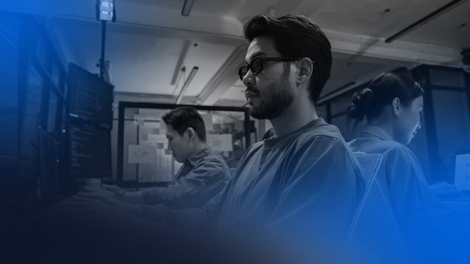 Equipe de desenvolvedores trabalhando em monitores com código, representando a prática de engenharia de software agêntica