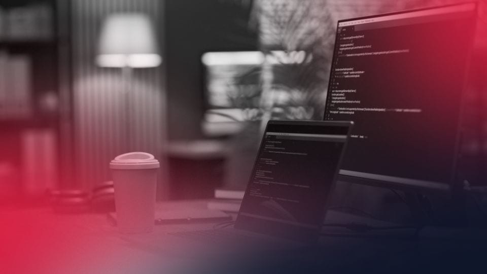 Estação de trabalho com código em monitor e café, simbolizando o fluxo de desenvolvimento em engenharia agêntica