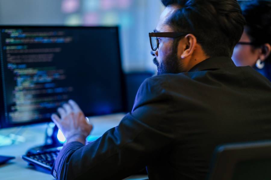 Engenheiro revisando código em monitor azul, representando a supervisão humana essencial na engenharia agêntica