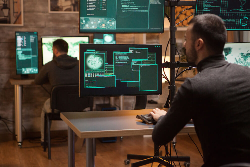 Profissionais monitoram múltiplas telas com códigos e sistemas de segurança, representando a aplicação do conceito de security by design.