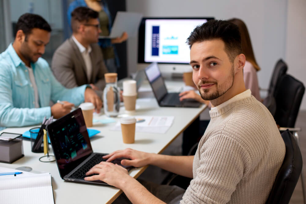 Profissionais de tecnologia trabalhando em equipe com notebooks em ambiente corporativo, ilustrando o modelo de body shop ou outsourcing de TI.